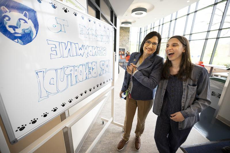 Two women stand next to a white board with a welcome message.